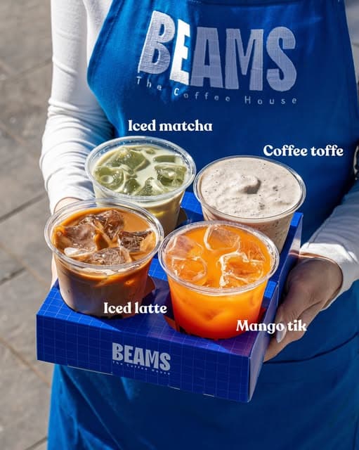 A barista in a Beams apron holding a tray of iced drinks